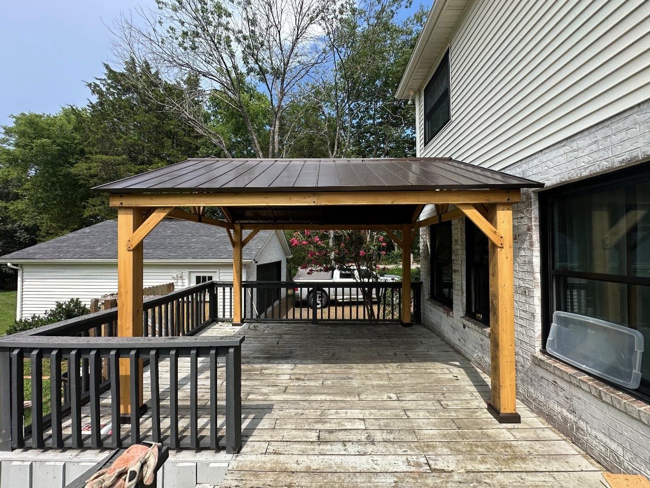 Cedar gazebo with a dark metal hip roof built on a raised deck beside a house