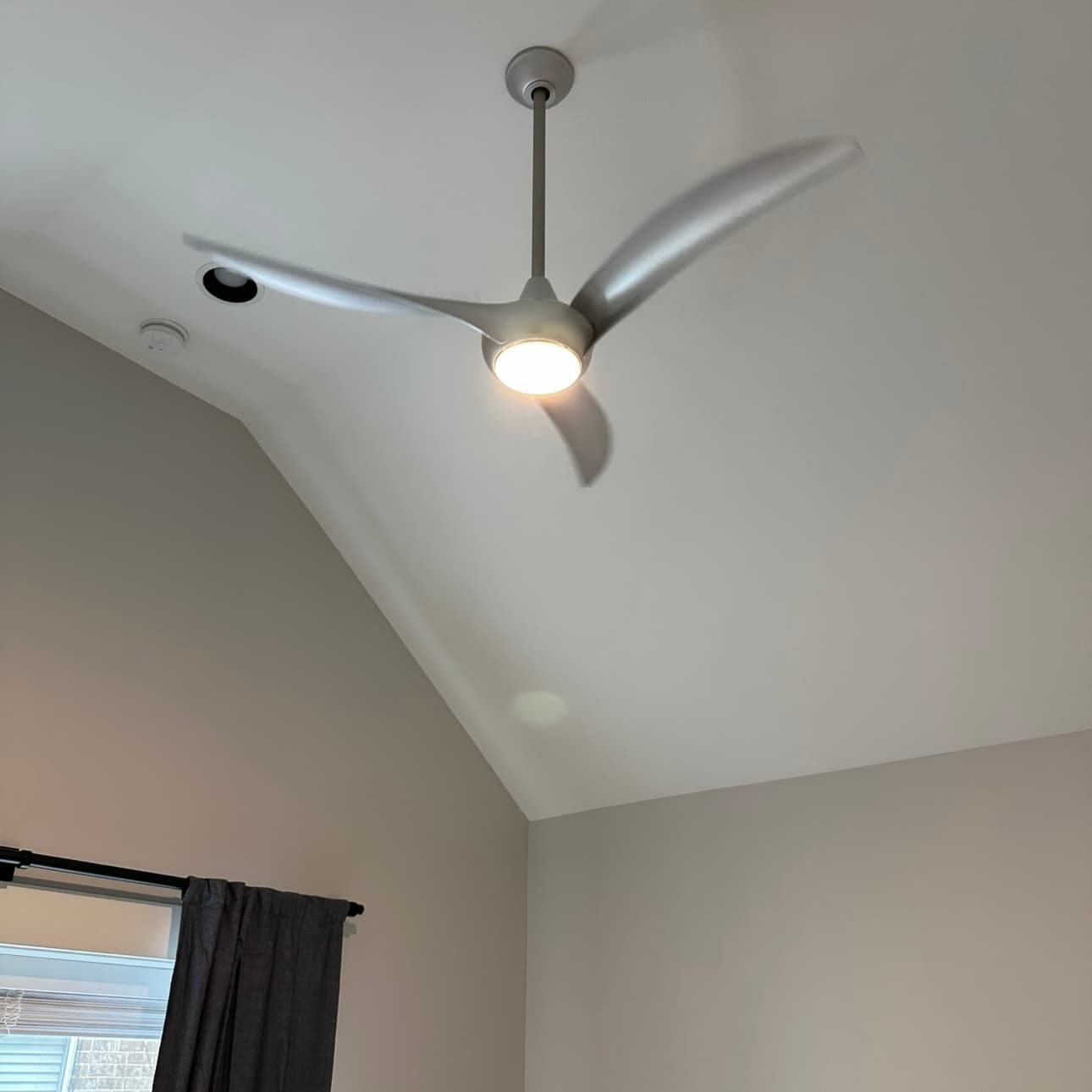 Three-blade ceiling fan with an integrated light, installed on a downrod under a vaulted ceiling
